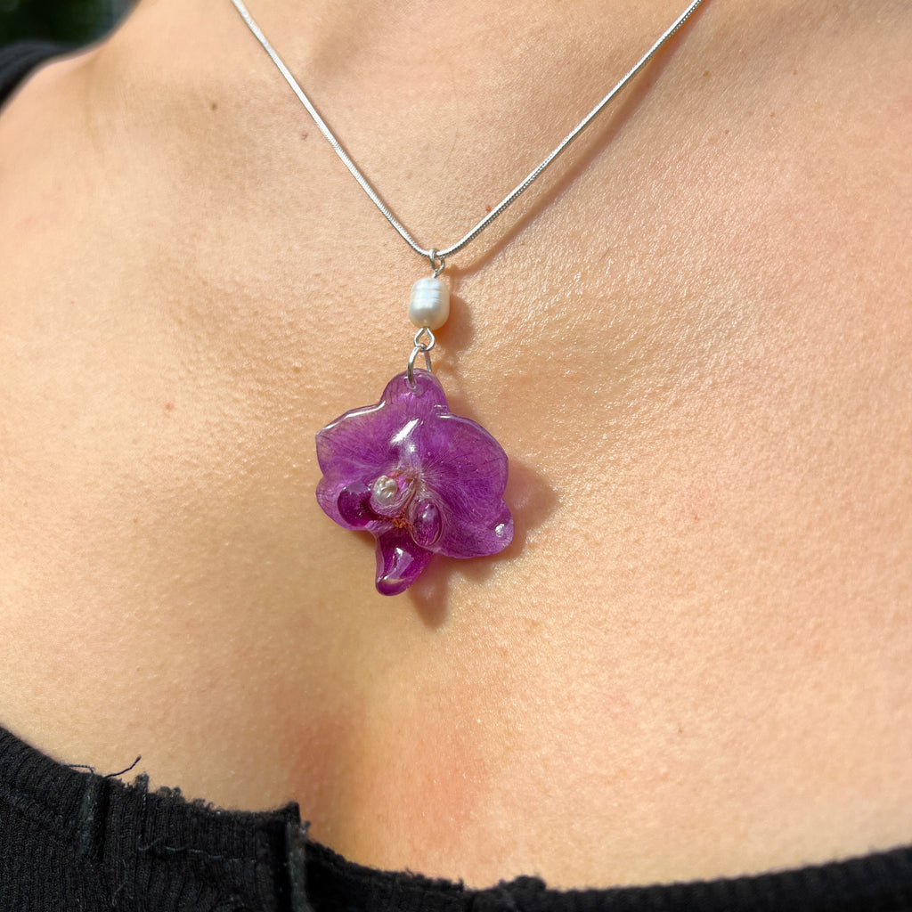 Necklace with a purple pendant and pearl on a person wearing a black top.
